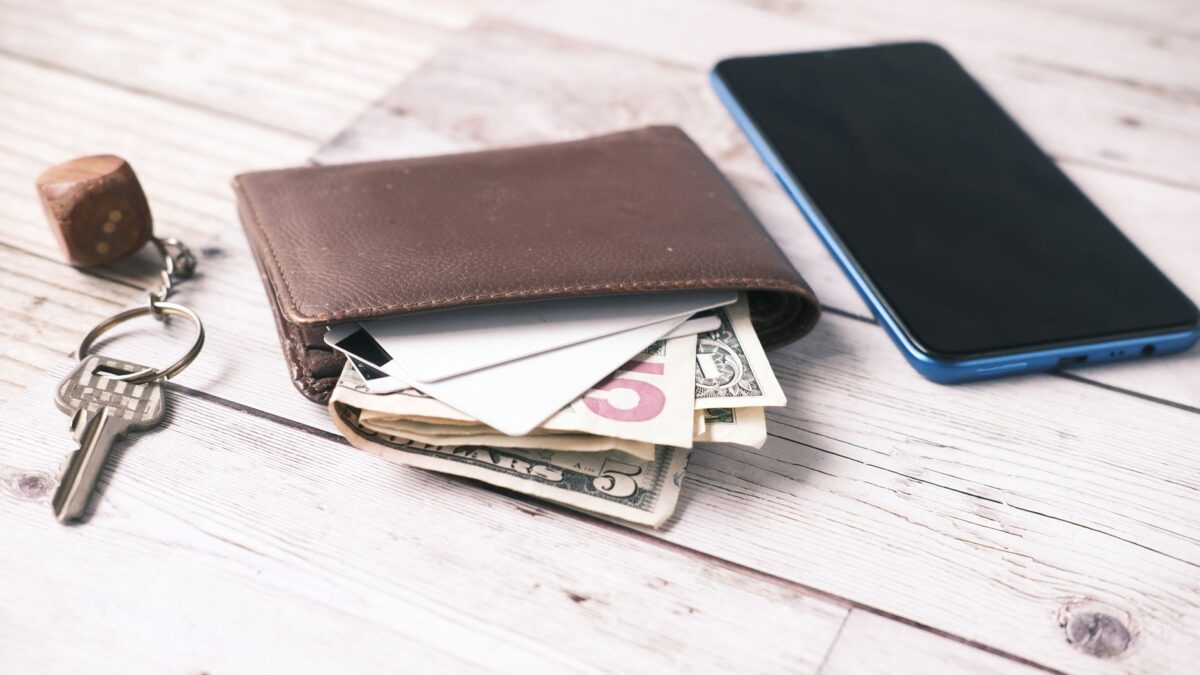 Close-up of a wallet with cash, smartphone, and keys on a wooden surface.