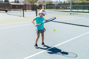 A young girl practicing tennis on an outdoor court on a sunny day, showing skill and focus.