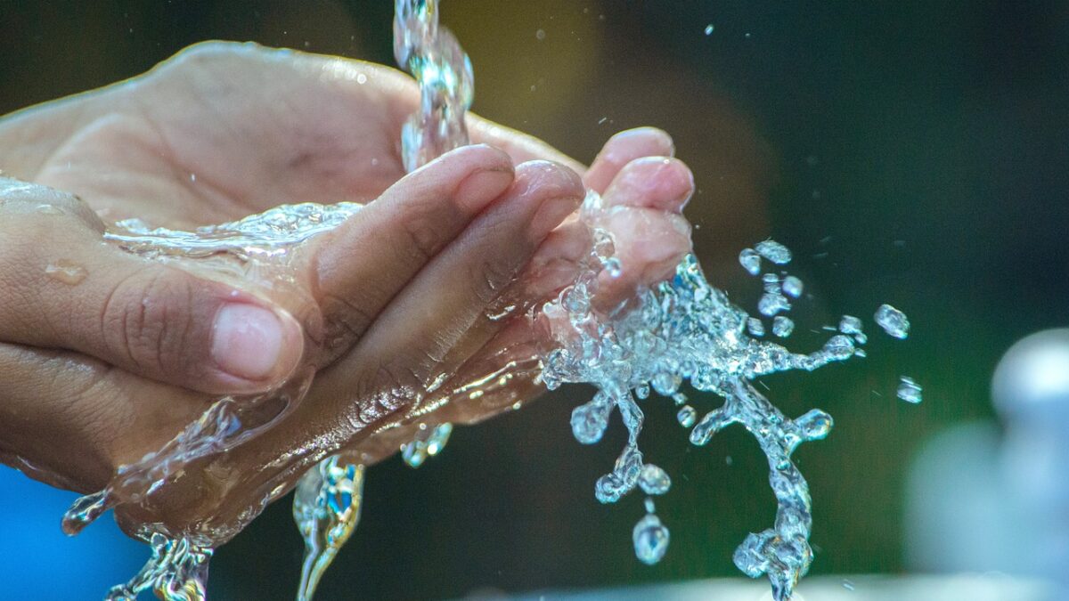 Deux mains sous un jet d'eau claire, avec des éclaboussures et des gouttelettes en mouvement sur fond sombre et flou.