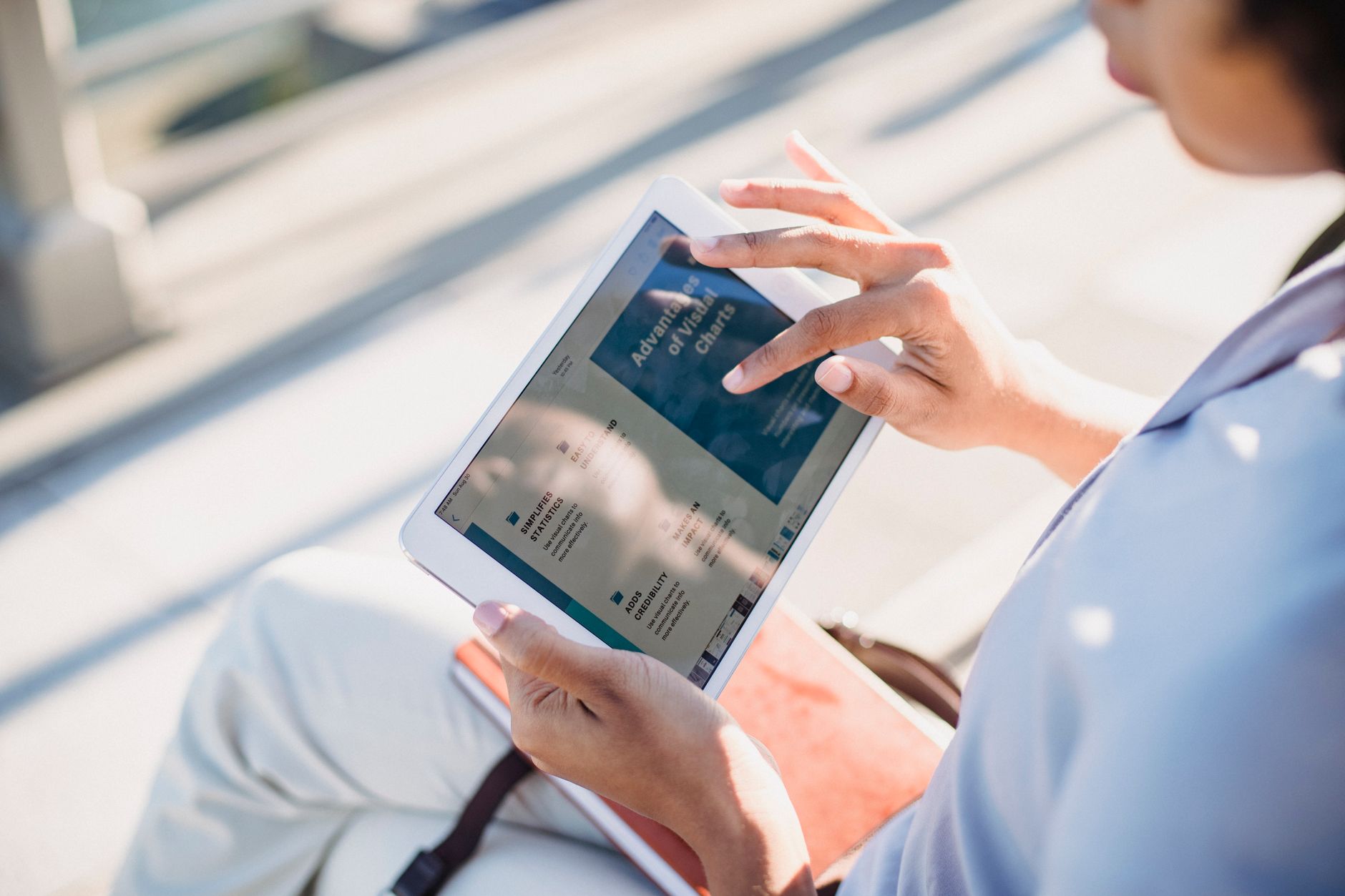 A person holding a white digital tablet showing a presentation on the screen outdoors.